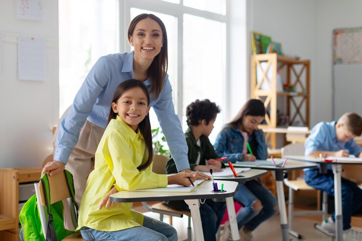 maestra-alegre-trabajando-nina-escuela-primaria-escritorio-maestra-feliz-nina-sonriendo_726520-457